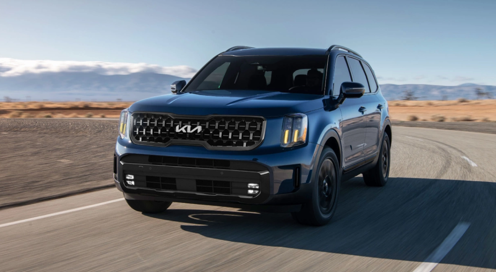 A dark blue 2025 Kia Telluride for sale driving on an open highway.