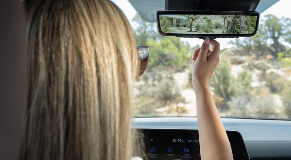 A woman using the review mirror in a 2025 Kia Telluride for sale near Golden Valley