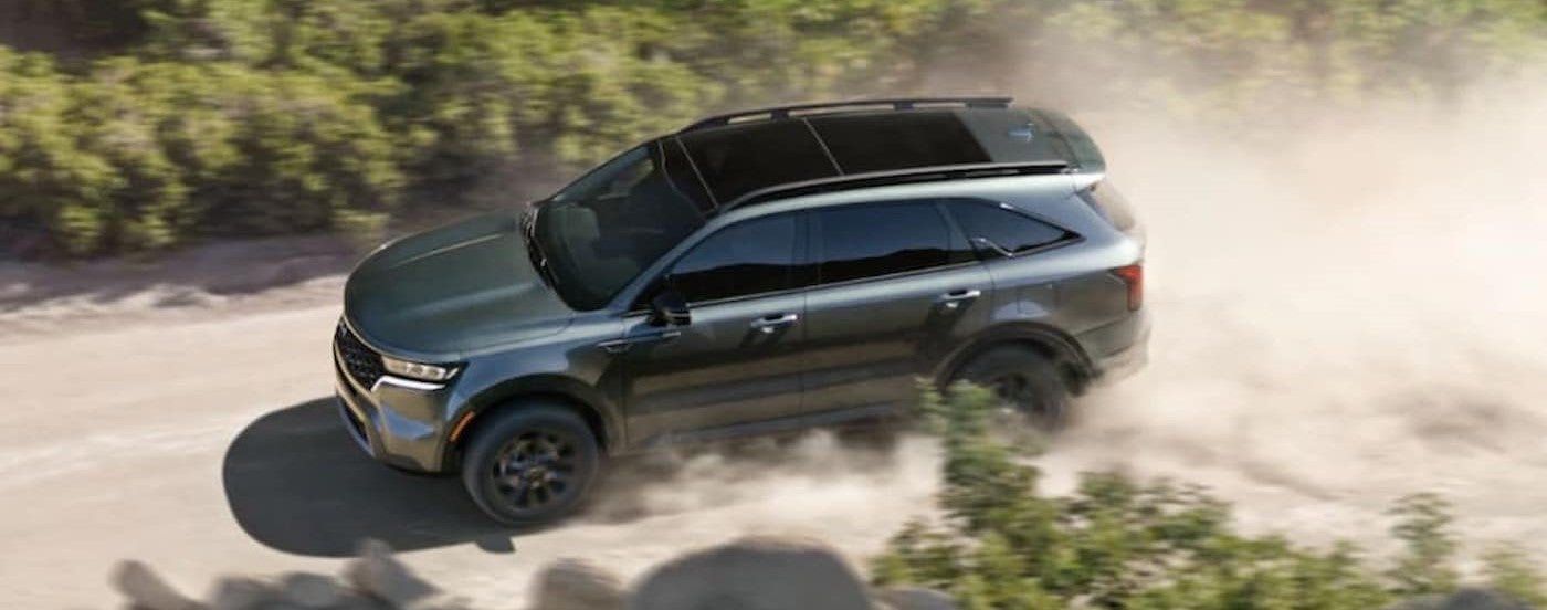 A green 2023 Kia Sorento for sale driving on a dirt road.