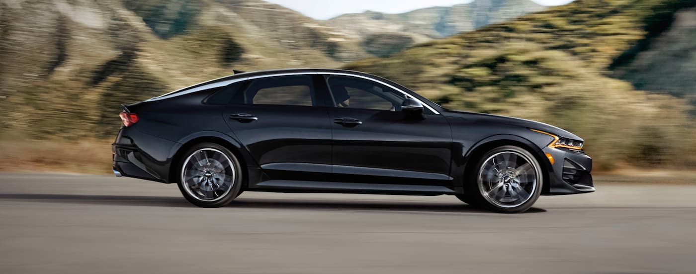 A black 2021 Kia K5 driving on an open road.